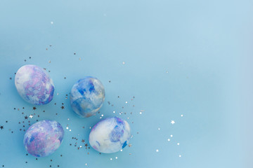 Colorful space-colored Easter eggs with sequins on a blue background. Happy Easter card with copy space for text. The concept of backgrounds for Easter. top view