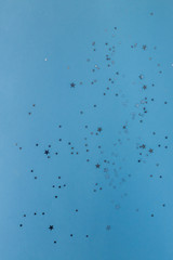 Star shaped silver sequins over classic blue background. Copy space.Holiday background for a greeting card. Top view, holiday concept.