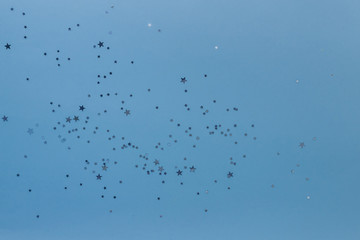 Fototapeta premium Star shaped silver sequins over classic blue background. Copy space.Holiday background for a greeting card. Top view, holiday concept.