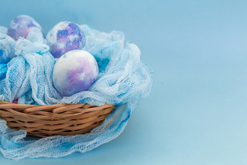 Easter basket with colorful cosmic eggs close-up on a blue background. Happy Easter card with copy space for text.