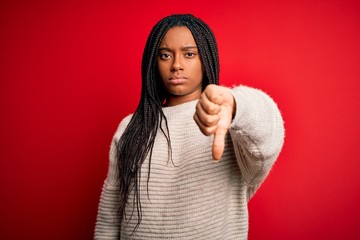 Young african american woman wearing casual winter sweater over red isolated background looking unhappy and angry showing rejection and negative with thumbs down gesture. Bad expression.