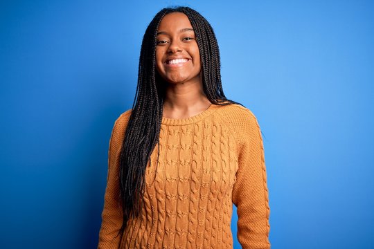 Young african american woman wearing casual yellow sweater standing over blue isolated background with a happy and cool smile on face. Lucky person.