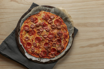 Overhead photography of a homemade pepperoni and sausage pizza on metal tray with a black napkin in a wooden table