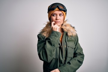 Young beautiful skier woman with blue eyes wearing snow sportswear and ski goggles with hand on chin thinking about question, pensive expression. Smiling with thoughtful face. Doubt concept.