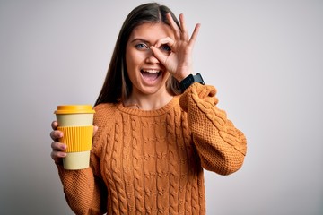 Young beautiful woman with blue eyes drinking cup of takeaway coffee over isolated background with happy face smiling doing ok sign with hand on eye looking through fingers