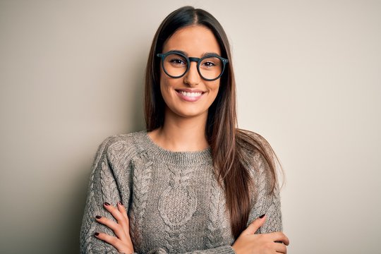 Young beautiful brunette woman wearing casual sweater and glasses over white background happy face smiling with crossed arms looking at the camera. Positive person.