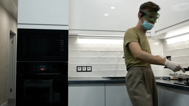 man in a medical mask and glasses in the kitchen is dancing and fooling around, self-isolation and quarantine.