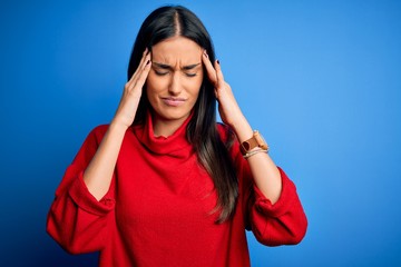 Fototapeta premium Young beautiful brunette woman wearing red casual sweater over isolated blue background suffering from headache desperate and stressed because pain and migraine. Hands on head.
