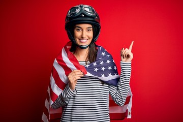 Young beautiful patriotic motorcyclist woman wearing moto helmet and united states flag surprised with an idea or question pointing finger with happy face, number one
