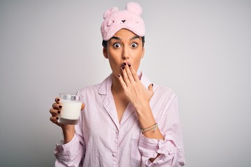 Young beautiful woman wearing pajama and sleep mask drinking glass of healthy milk cover mouth with hand shocked with shame for mistake, expression of fear, scared in silence, secret concept