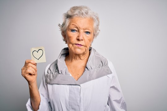 Senior beautiful grey-haired woman holding reminder paper heart over white background with a confident expression on smart face thinking serious