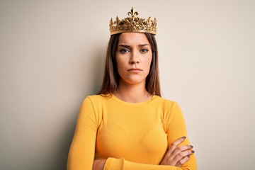 Young beautiful brunette woman wearing golden queen crown over white background skeptic and...