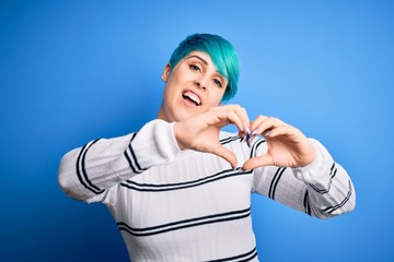 Young beautiful woman with blue fashion hair wearing casual sweater standing at studio smiling in love doing heart symbol shape with hands. Romantic concept.