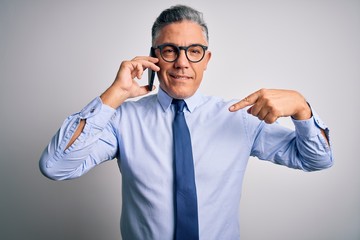 Middle age handsome grey-haired business man having conversation talking on the smartphone with surprise face pointing finger to himself