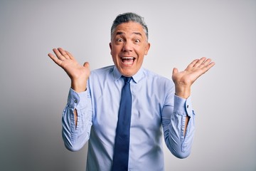 Middle age handsome grey-haired business man wearing elegant shirt and tie celebrating crazy and amazed for success with arms raised and open eyes screaming excited. Winner concept