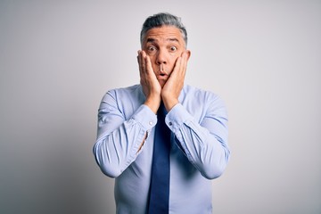 Middle age handsome grey-haired business man wearing elegant shirt and tie afraid and shocked, surprise and amazed expression with hands on face