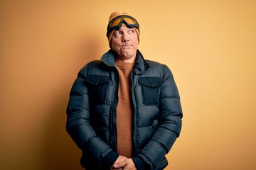 Middle age handsome grey-haired skier man on vacation wearing ski goggles smiling looking to the side and staring away thinking.