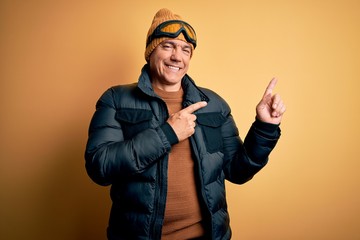 Middle age handsome grey-haired skier man on vacation wearing ski goggles smiling and looking at the camera pointing with two hands and fingers to the side.