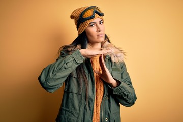 Young beautiful hispanic woman wearing ski glasses and coat for winter weather Doing time out gesture with hands, frustrated and serious face