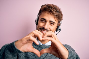 Young call center agent man with beard wearing headset over isolated pink background smiling in...