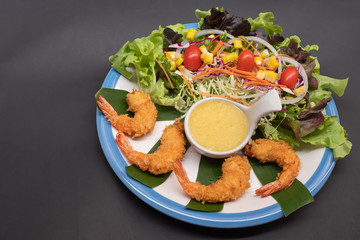 Shrimp tempura and salad of fresh vegetables close-up on a plate on black background. horizontal view from above