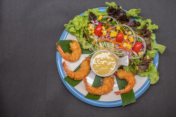 Shrimp tempura and salad of fresh vegetables close-up on a plate on black background. horizontal view from above