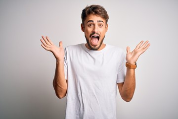 Fototapeta premium Młody przystojny mężczyzna z brodą ubrany w casualową koszulkę stojącą na białym tle świętujący szalony i zdumiony sukcesem z podniesionymi rękami i otwartymi oczami krzyczącymi podekscytowany. Koncepcja zwycięzcy
