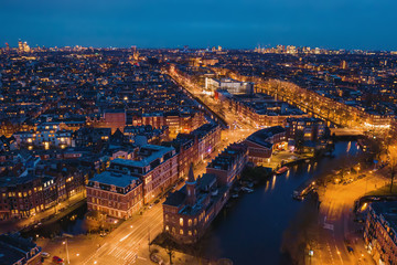 Aerial panoramic view of evening Amsterdam with water canals, illuminated roads and historic buildings, The Netherlands.