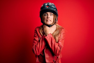 Young beautiful brunette motrocyclist woman wearing moto helmet over red background shouting and suffocate because painful strangle. Health problem. Asphyxiate and suicide concept.