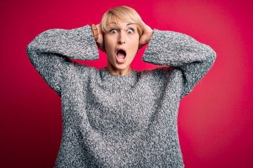 Young blonde woman with modern short hair wearing casual sweater over pink background Crazy and scared with hands on head, afraid and surprised of shock with open mouth