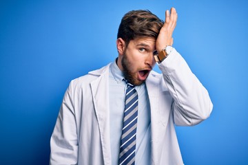 Young blond therapist man with beard and blue eyes wearing coat and tie over background surprised with hand on head for mistake, remember error. Forgot, bad memory concept.