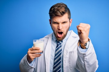 Young blond doctor man with beard and blue eyes wearing coat drinking glass of milk annoyed and frustrated shouting with anger, crazy and yelling with raised hand, anger concept