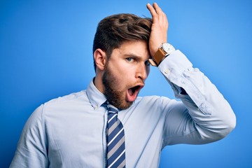 Young blond businessman with beard and blue eyes wearing elegant shirt and tie standing surprised...