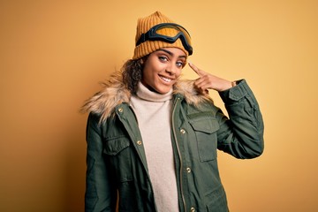 Young african american afro skier girl wearing snow sportswear and ski goggles Smiling pointing to head with one finger, great idea or thought, good memory