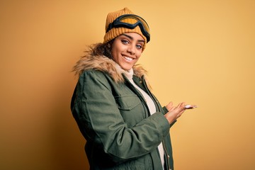 Young african american afro skier girl wearing snow sportswear and ski goggles Inviting to enter smiling natural with open hand