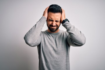 Young handsome man with beard wearing casual sweater standing over white background suffering from headache desperate and stressed because pain and migraine. Hands on head.