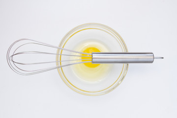 metal whisk and chicken yolk in a glass bowl