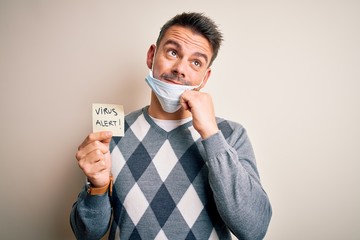 Young handsome man wearing medical mask holding paper with virus alert message serious face thinking about question, very confused idea