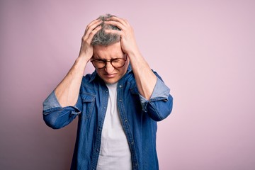 Young handsome modern man wearing glasses and denim jacket over pink isolated background suffering from headache desperate and stressed because pain and migraine. Hands on head.