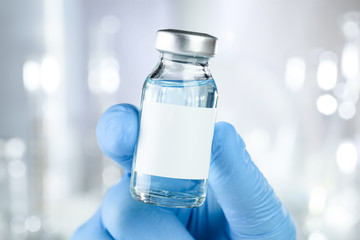 Healthcare concept with a hand in blue medical gloves holding a vaccine vial with blue liquid and...