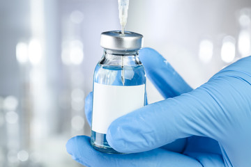 Healthcare concept with a hand in blue medical gloves holding a vaccine vial with blue liquid and...