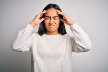 Young beautiful asian woman wearing casual sweater standing over white background suffering from headache desperate and stressed because pain and migraine. Hands on head.