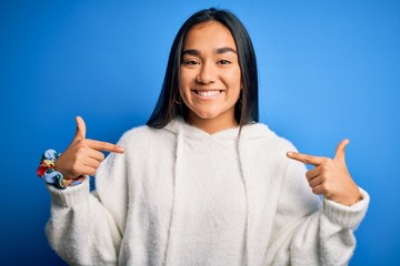 Young beautiful asian sportswoman wearing sweatshirt standing over isolated blue background looking confident with smile on face, pointing oneself with fingers proud and happy.