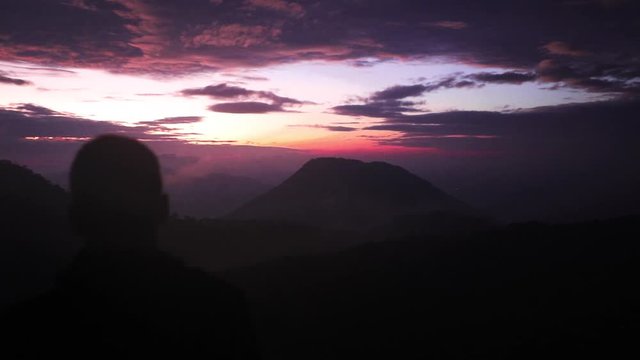 Medium closeup shot showing the silhouette of a man taking a picture with his phone of the colourful purple sunrise in the mountains