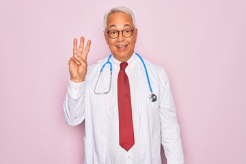 Middle age senior grey-haired doctor man wearing stethoscope and professional medical coat showing and pointing up with fingers number three while smiling confident and happy.