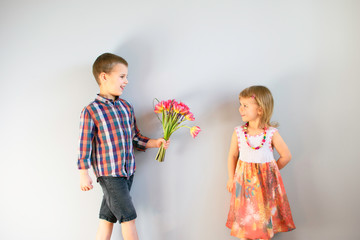 The little boy in plaid shirt gives small little girl in bright summer dress a bouquet of tulips.