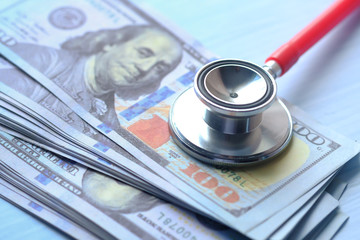 Stack of cash dollars and stethoscope on blue background