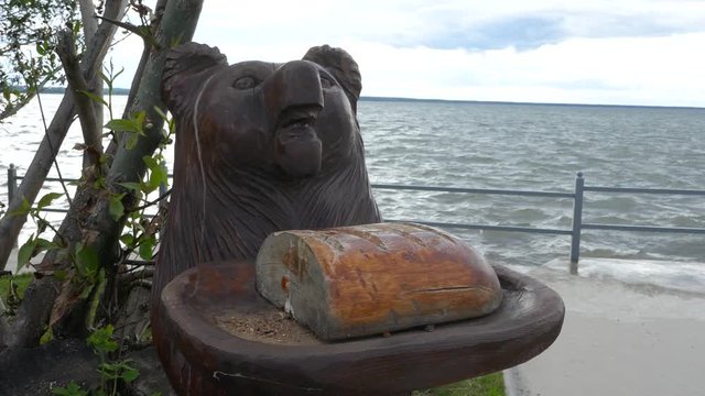 Wooden bear offering bread with sea water in background