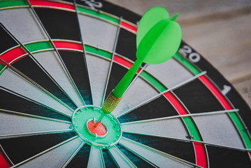 Close up shot of the green dart arrow hit on bull eyes of dartboard to represent that the business reached the target of company with Monochrome tone picture style. target and goal ass concept.
