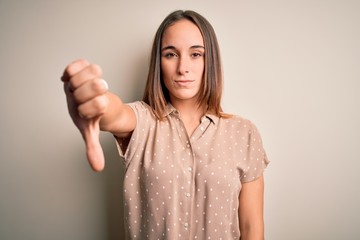 Young beautiful woman wearing casual shirt standing over isolated white background looking unhappy and angry showing rejection and negative with thumbs down gesture. Bad expression.
